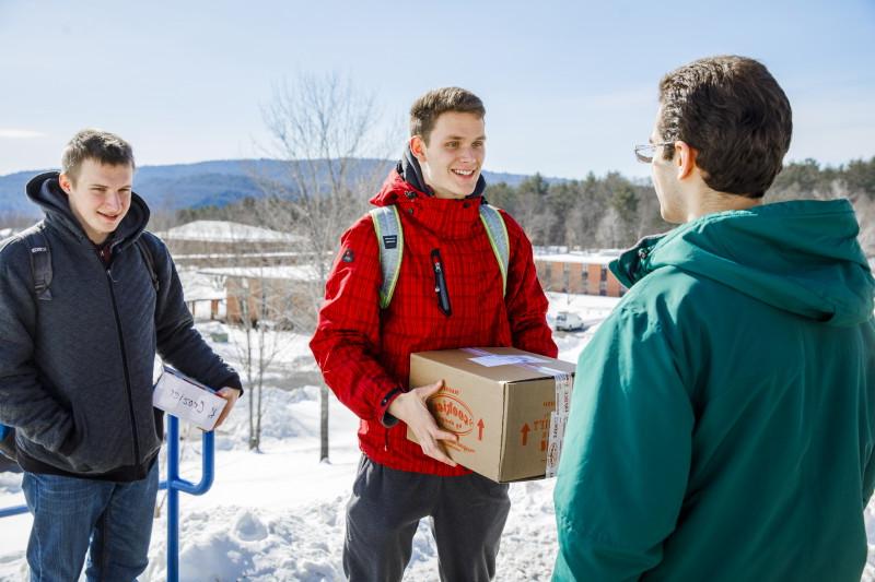 Photograph of winter scene of two Landmark College students holding mailed packages while third student looks on.
